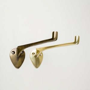 May include: Two metal towel bars, one in a brass finish and one in an antique brass finish. Both bars have a curved design and are mounted to a wall.