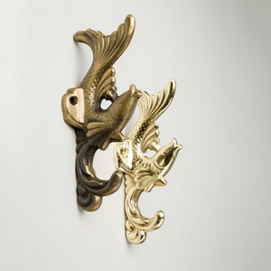 Può includere: Due ganci da parete decorativi a forma di pesce. Il gancio a sinistra è in bronzo e il gancio a destra è in oro.