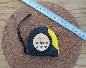 Peut inclure: Un mètre ruban jaune et noir avec une plaque en bois sur laquelle est inscrit "Papa tu es le mètre de mon" avec un petit symbole de cœur.