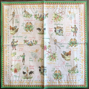 May include: A white napkin with a green border features a 12-day Christmas countdown illustration. Each day is numbered with a corresponding festive image and rhyme. The text "On the first day of Christmas, my true love sent to me..." is printed at the bottom.