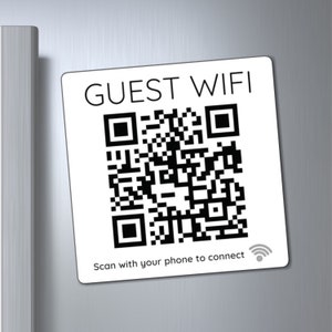 May include: White square sign with black text that reads "GUEST WIFI" and a black and white QR code. Below the QR code is the text "Scan with your phone to connect" and a black wifi symbol.