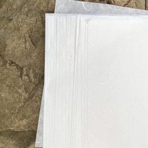 May include: A stack of white textured paper sheets. The paper has a slightly rough, handmade look.