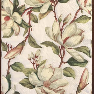 May include: A rectangular paper napkin featuring a repeating botanical pattern of white magnolia flowers with cream centers, dark green leaves, and brown branches set against a stark white background with a subtle embossed texture throughout.