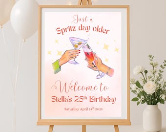 May include: A framed sign on an easel with the text "Just a Spritz day older" and "Welcome to Stella's 25th Birthday". The illustration shows two hands toasting cocktails. The date "Saturday April 14th 2025" is also displayed.