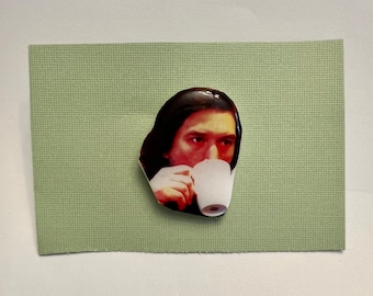May include: A close-up of a man with dark hair drinking from a white mug. He is wearing a dark shirt and has a serious expression on his face.