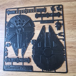 May include: A black plastic sprue sheet with the words "Millennium Falcon" printed on it. The sheet contains various parts for building a model of the Millennium Falcon spaceship.