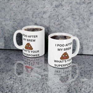 May include: Two white coffee mugs with black text and a cartoon poop emoji. The text on the mugs reads "I poo after my brew what's your superpower" and "Poo after my brew what's your superpower".