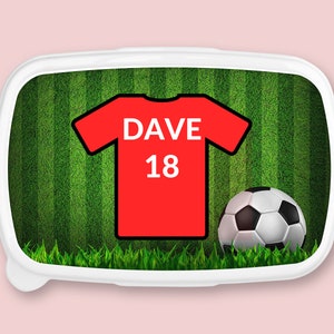 May include: A white lunchbox with a green and white striped background. A red football shirt with the name "DAVE" and the number "18" is on the background. A black and white football is in the bottom right corner.