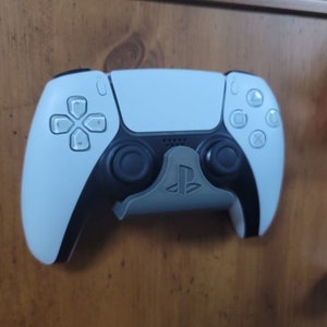May include: A white PlayStation 5 DualSense controller with a black PlayStation logo on a wall mount.