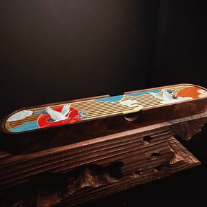 May include: An elongated, oval-shaped wooden tea tray featuring a slatted surface. The tray is decorated with a vibrant graphic print of white cranes, a large red sun, and blue stylised clouds against a natural wood grain background.