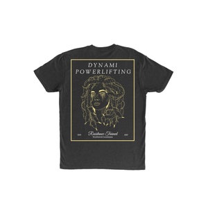 Könnte beinhalten: Dunkelgraues T-Shirt mit einer goldfarbenen Grafik eines Frauengesichts mit schlangenartigem Haar, innerhalb eines goldenen rechteckigen Rahmens. Der Text "DYNAMi POWERLIFTING" befindet sich über der Grafik. Darunter steht "Resistance Trained Southwest Louisiana".