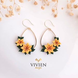 May include: A pair of gold hoop earrings with a teardrop shape. Each earring is decorated with three yellow and green polymer clay flowers.