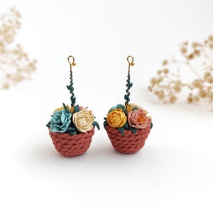 May include: A pair of earrings featuring small terracotta pots with colorful polymer clay flowers. The pots have a woven texture and are attached to gold-colored hooks.