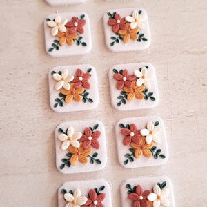 May include: Ten small square tiles with a floral design. Each tile features three flowers in shades of white, orange, and red with green leaves.