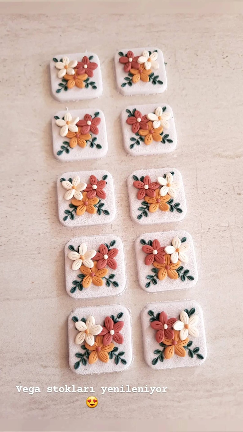 May include: Ten small square tiles with a floral design. Each tile features three flowers in shades of white, orange, and red with green leaves.