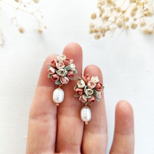 May include: A pair of delicate earrings featuring a cluster of pastel pink, white, and green polymer clay flowers with a single pearl drop on each earring.