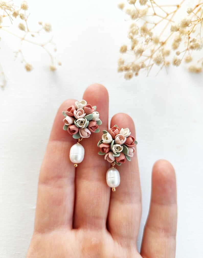 May include: A pair of delicate earrings featuring a cluster of pastel pink, white, and green polymer clay flowers with a single pearl drop on each earring.