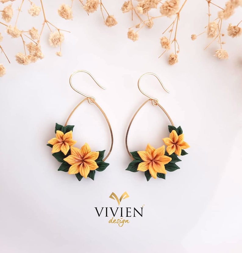 May include: A pair of gold hoop earrings with a teardrop shape. Each earring is decorated with three yellow and green polymer clay flowers.