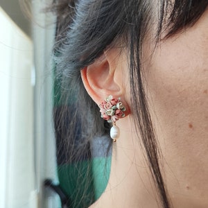May include: A pair of earrings with a cluster of pink, green, and white flowers and a single pearl dangling from the bottom.