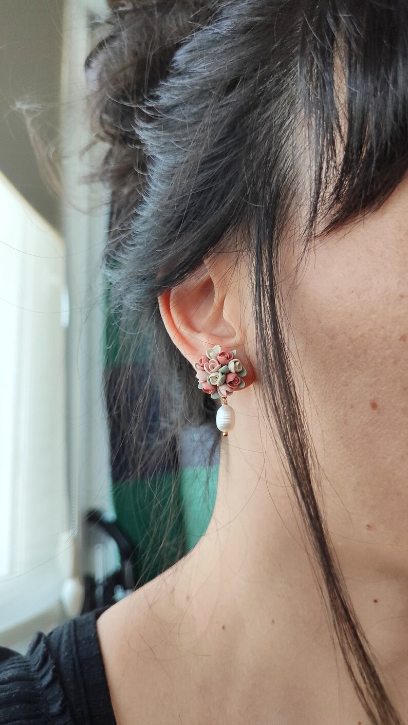 May include: A pair of earrings with a cluster of pink, green, and white flowers and a single pearl dangling from the bottom.