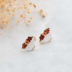 May include: A pair of white ceramic earrings with a gold rim and a cluster of orange, red, and pink flowers.