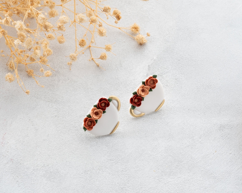 May include: A pair of white ceramic earrings with a gold rim and a cluster of orange, red, and pink flowers.