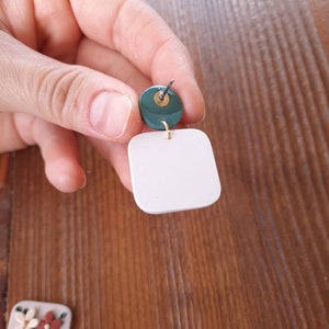 May include: A pair of white square earrings with a green circle accent. The earrings are made of polymer clay and have a gold-colored wire.