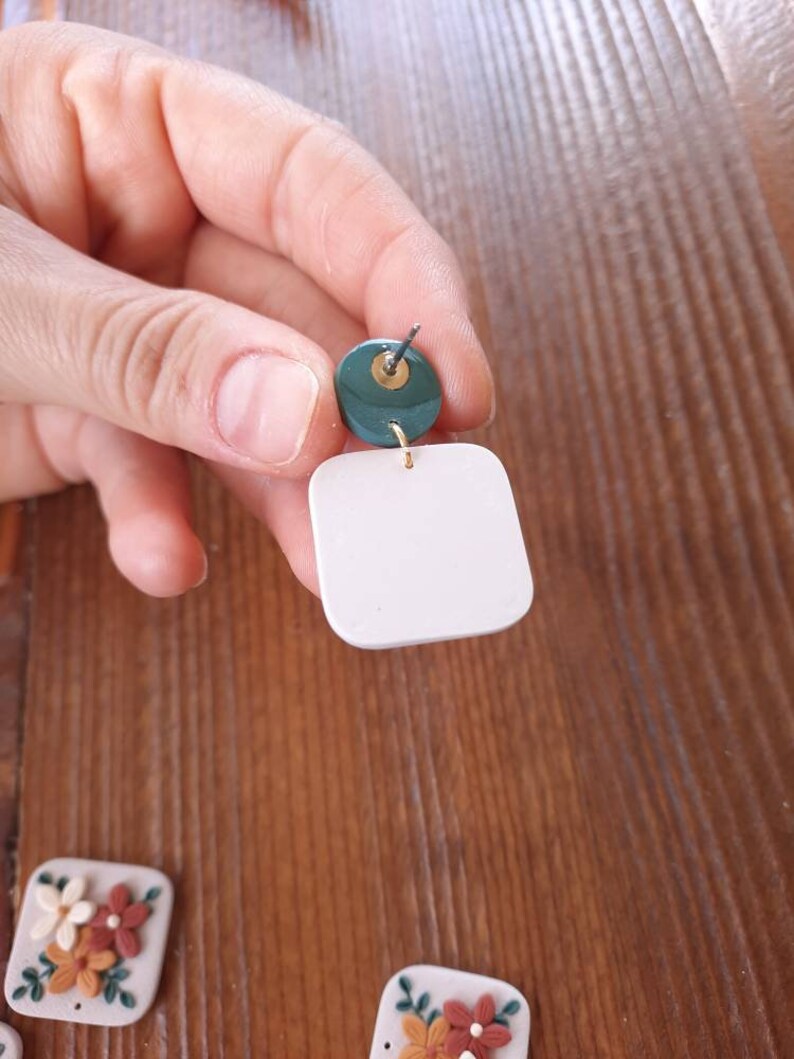 May include: A pair of white square earrings with a green circle accent. The earrings are made of polymer clay and have a gold-colored wire.