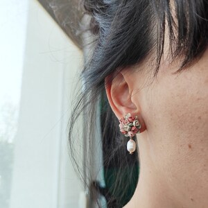 May include: A pair of earrings with a cluster of pink and green fabric flowers and a single pearl dangling from each earring.