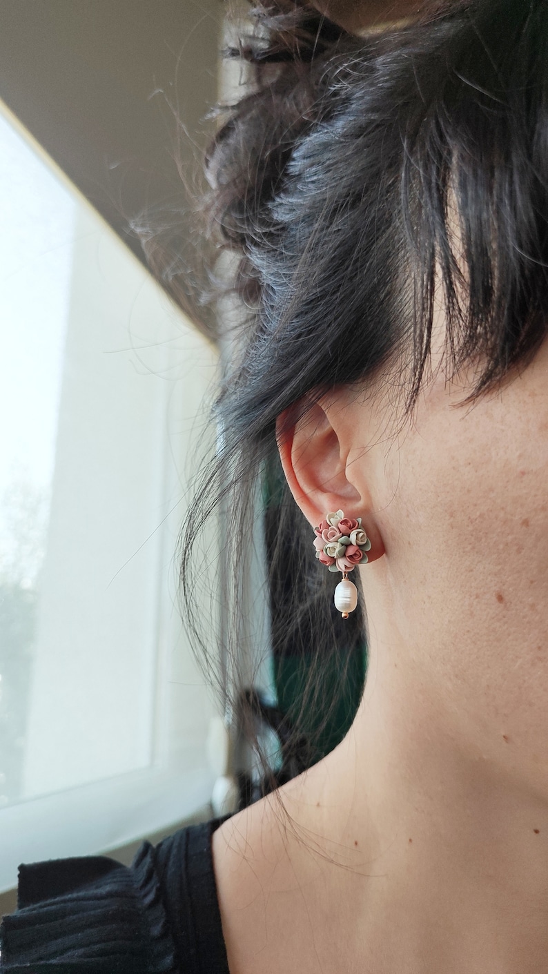 May include: A pair of earrings with a cluster of pink and green fabric flowers and a single pearl dangling from each earring.