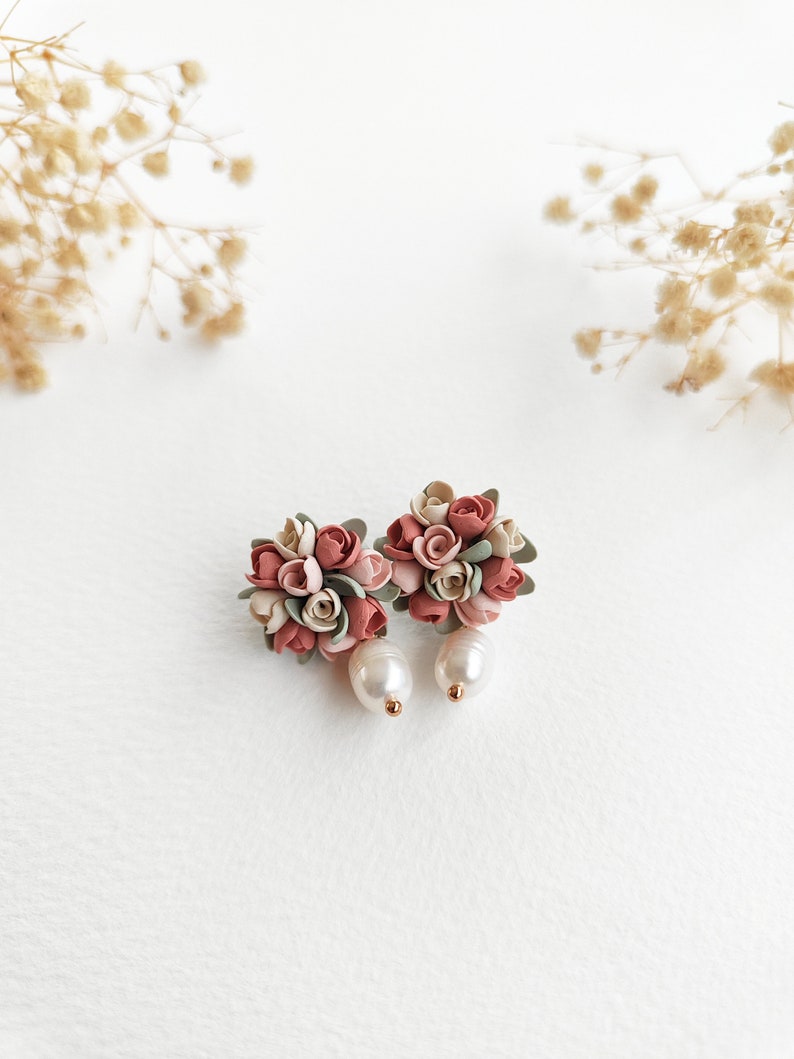 May include: A pair of floral earrings with pink, white, and green polymer clay flowers and a pearl dangle.