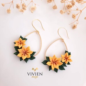 May include: A pair of gold hoop earrings with a teardrop shape. The hoops are adorned with yellow and green polymer clay flowers.