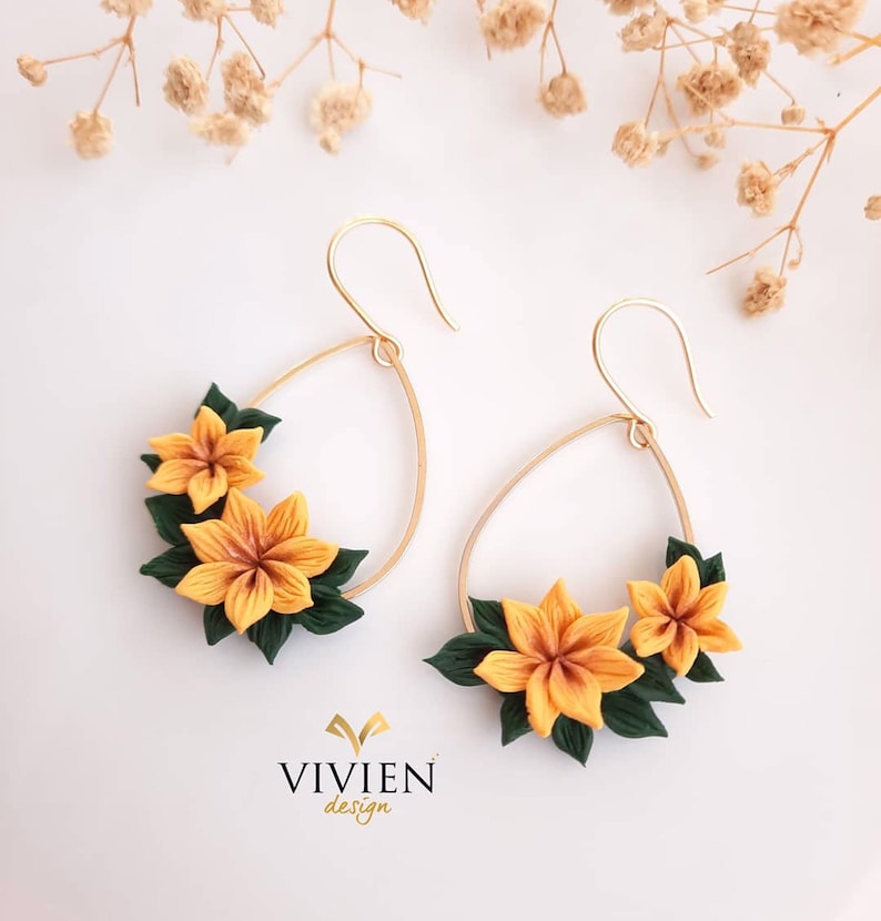 May include: A pair of gold hoop earrings with a teardrop shape. The hoops are adorned with yellow and green polymer clay flowers.