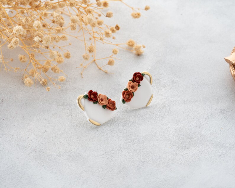 May include: A pair of white ceramic earrings with a gold rim and a floral design. The flowers are orange, red, and green.