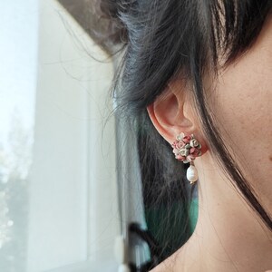 May include: A pair of floral earrings with a pearl dangle. The earrings are made of small pink, green, and white flowers.