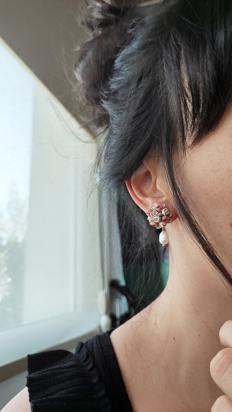 May include: A pair of floral earrings with a pearl dangle. The earrings are made of small pink, green, and white flowers.