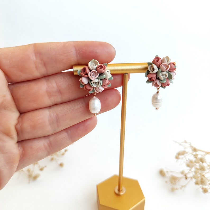 May include: A pair of dangle earrings with a cluster of pink, white, and green polymer clay flowers and a single pearl drop on each earring.