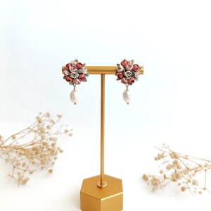May include: A pair of floral dangle earrings with a cluster of pink, white, and green polymer clay flowers and a single pearl drop on each earring.