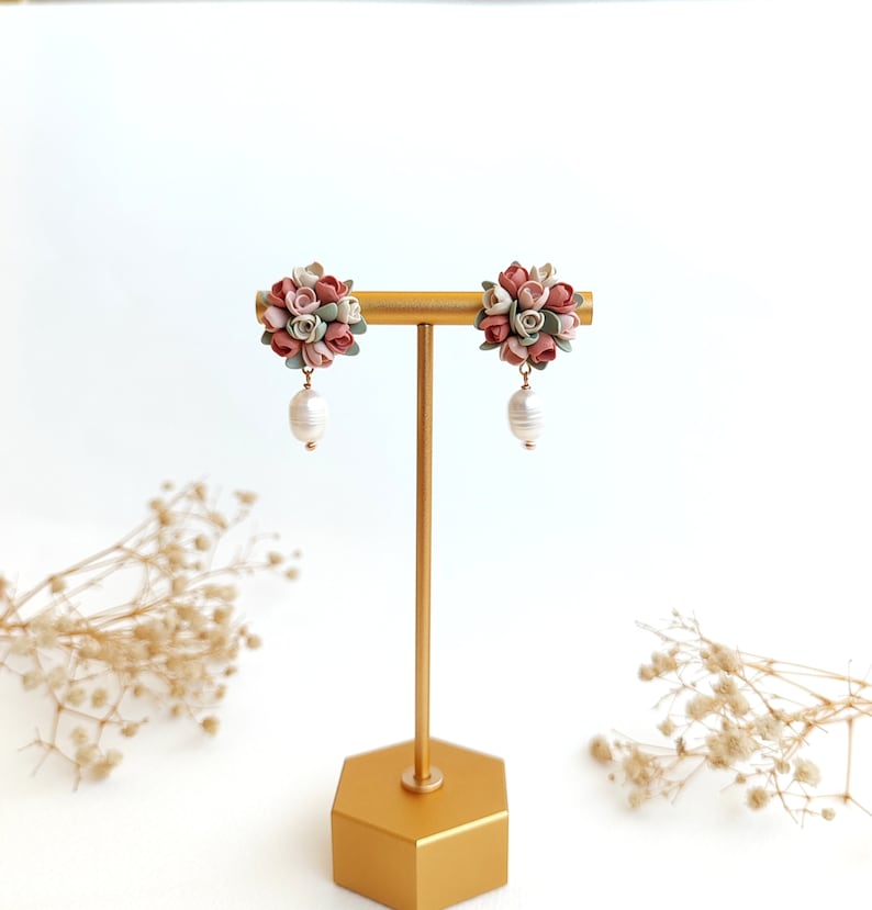 May include: A pair of floral dangle earrings with a cluster of pink, white, and green polymer clay flowers and a single pearl drop on each earring.