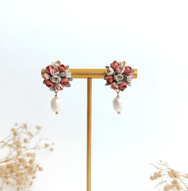 May include: A pair of dangle earrings with a cluster of pink, white, and green polymer clay flowers and a single pearl drop on each earring.