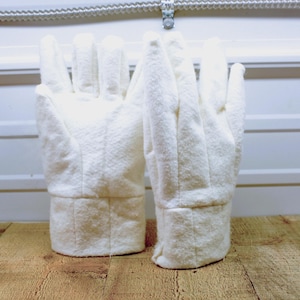 May include: A pair of off-white work gloves made of a textured fabric. The gloves have a cuff at the wrist and are designed to cover the entire hand and fingers. They are displayed on a wooden surface.