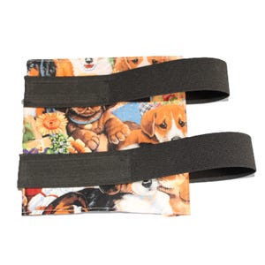 May include: A black and white fabric dog print pouch with two black elastic straps. The pouch is designed to hold a phone or other small items.