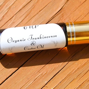 May include: A gold and brown glass roller bottle with a white label that reads "Organic Frankincense & Castor Oil".