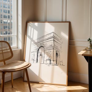 May include: A black and white line drawing of the Arc de Triomphe in Paris, France, framed in a light wood frame and hanging on a white wall.