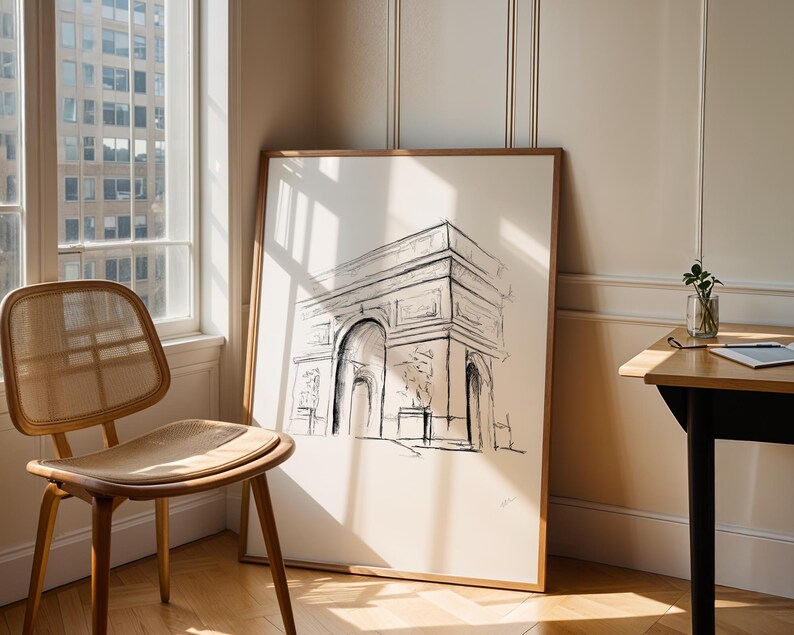 May include: A black and white line drawing of the Arc de Triomphe in Paris, France, framed in a light wood frame and hanging on a white wall.
