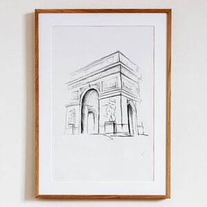 May include: A black and white pencil sketch of the Arc de Triomphe in Paris, France. The drawing is framed in a light wood frame.