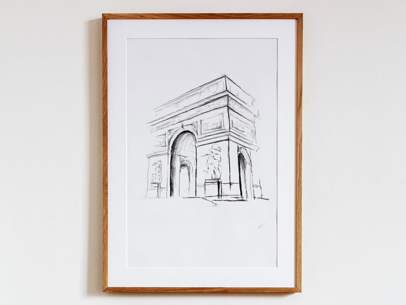 May include: A black and white pencil sketch of the Arc de Triomphe in Paris, France. The drawing is framed in a light wood frame.