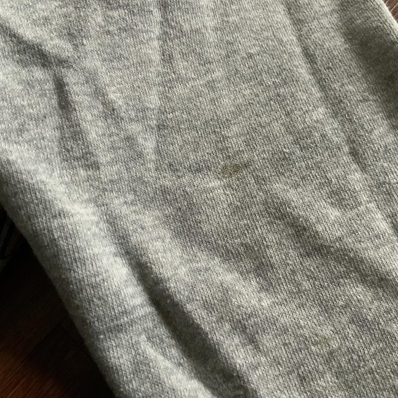 K&ouml;nnte beinhalten: Nahaufnahme eines hellgrauen Stoffes mit strukturierter Oberfl&auml;che. Der Stoff hat ein paar kleine, dunkle Flecken. Das Bild zeigt die Textur und Farbe des Materials.