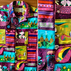 May include: A button-down shirt featuring a vibrant, multi-coloured tropical print. The design includes illustrations of pineapples, parrots, and abstract geometric patterns in shades of purple, pink, blue, yellow, and green. It has a collar and buttons.