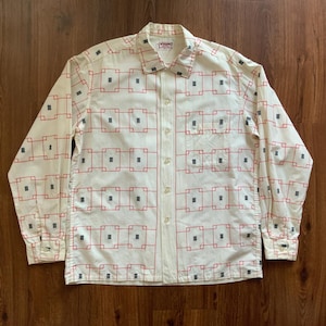 May include: Cream-colored button-down shirt with a geometric pattern of red squares and black rectangles. The long-sleeved shirt has a collared neckline, a chest pocket, and buttoned cuffs. The shirt is made of a lightweight fabric.